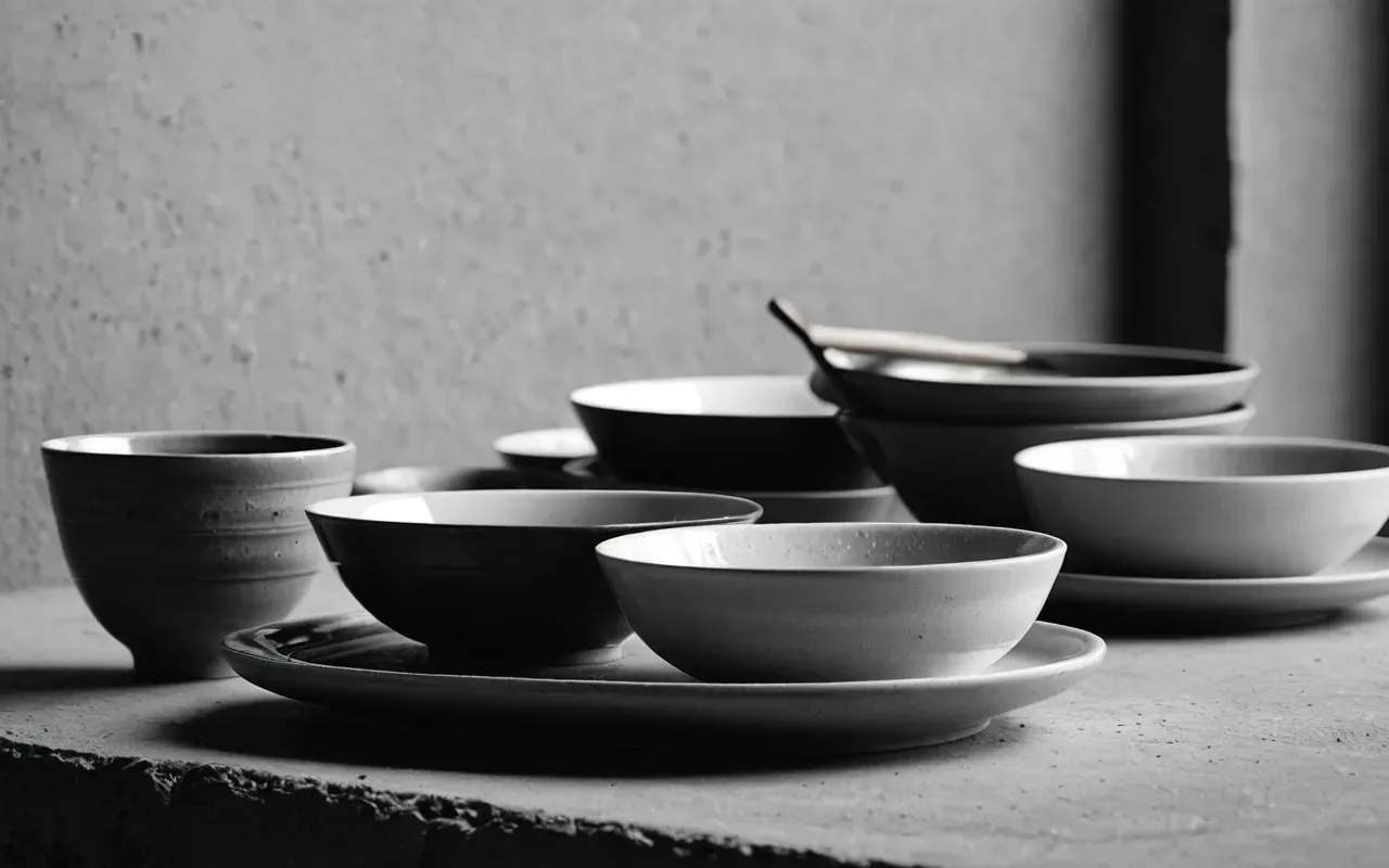 Clean editorial still life of ceramic dishware on a concrete surface, diffused soft light, monochrome neutral tones, no text